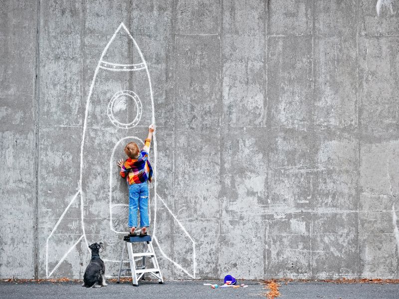 Little boy drawing a big rocket ship on the side of a building